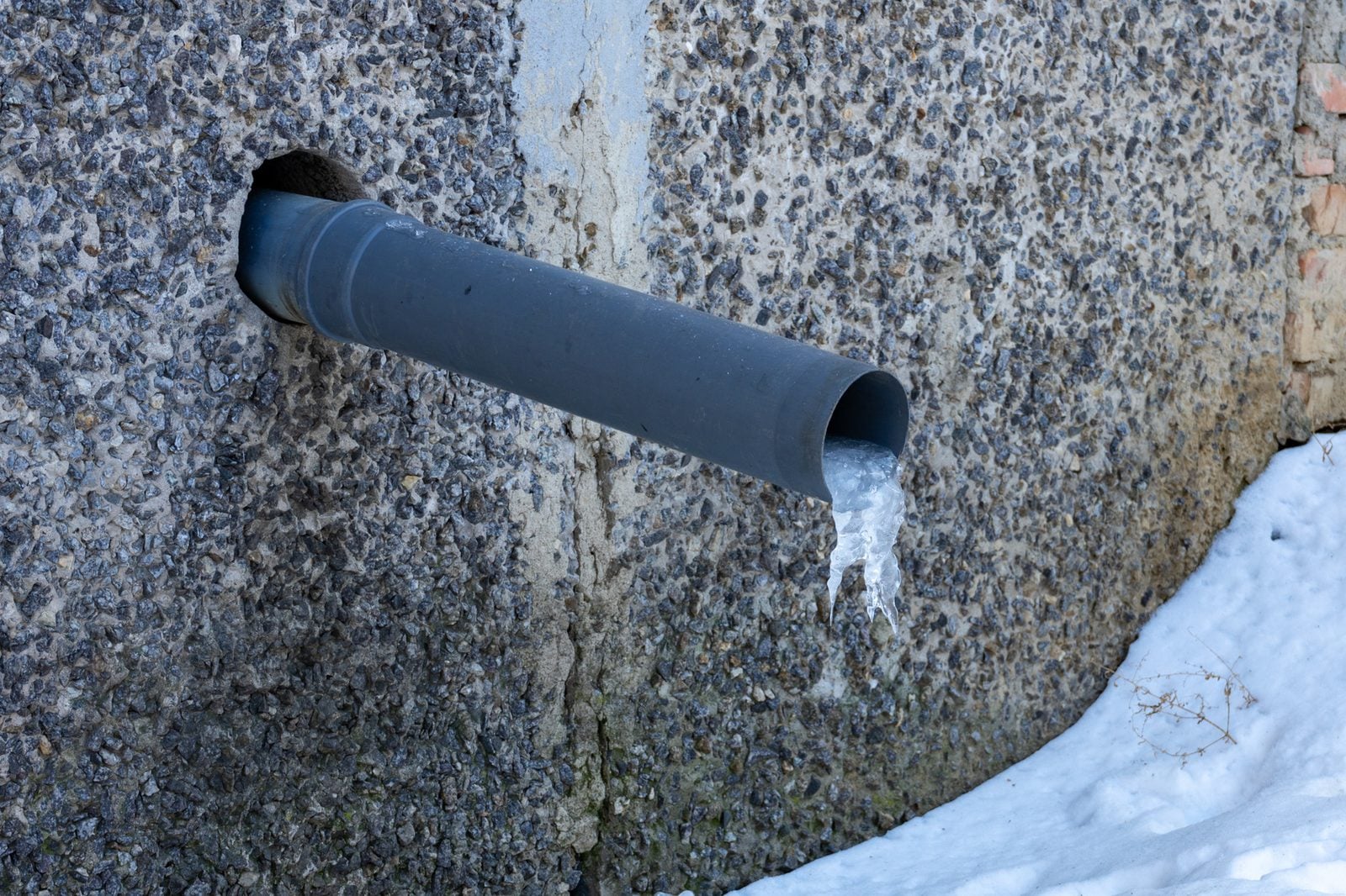 Frozen water pipe sticking out of a wall with ice